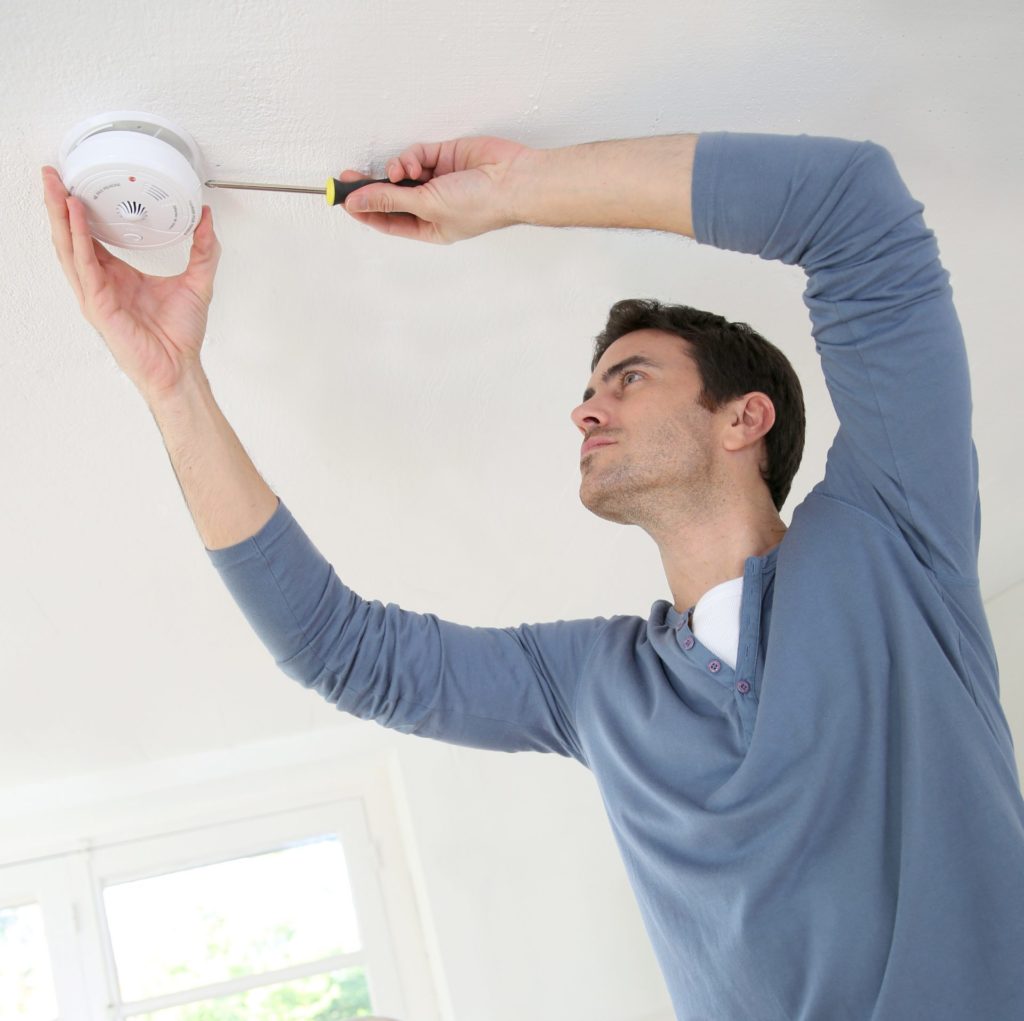 Man wearing blue jumper installing fire alarm system