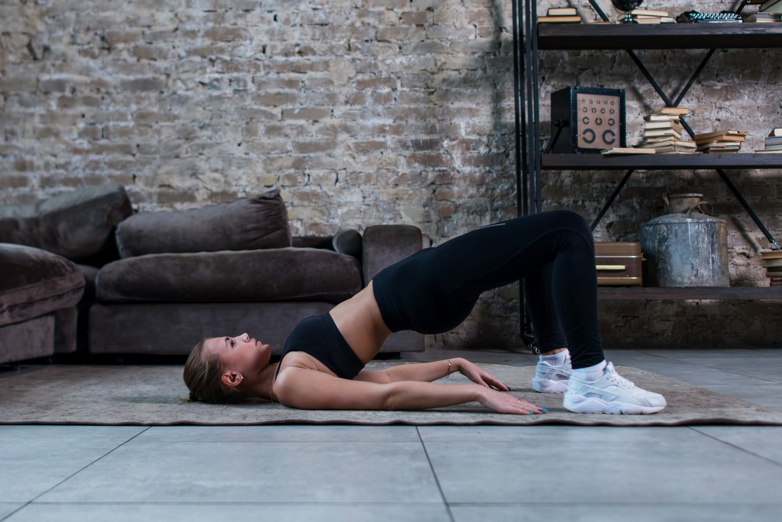 sporty girl doing floor hip raise or butt lift exercise lying on floor in her loft apartment