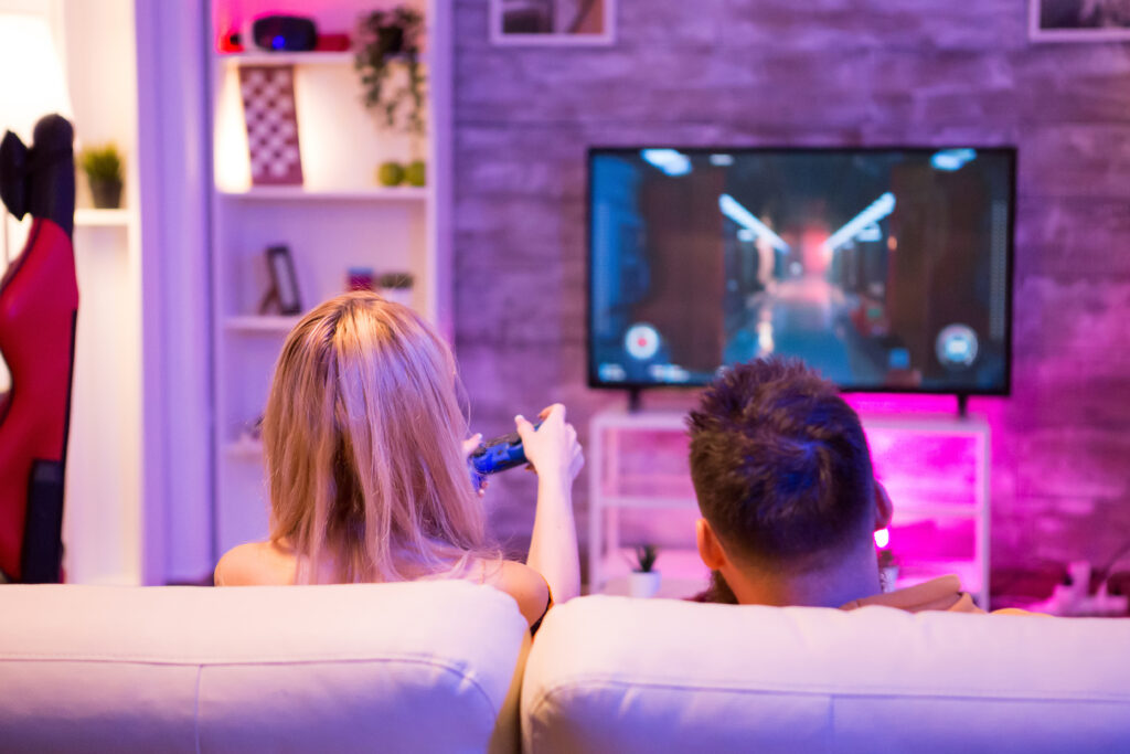 Back view of young couple relaxing playing online shooter games